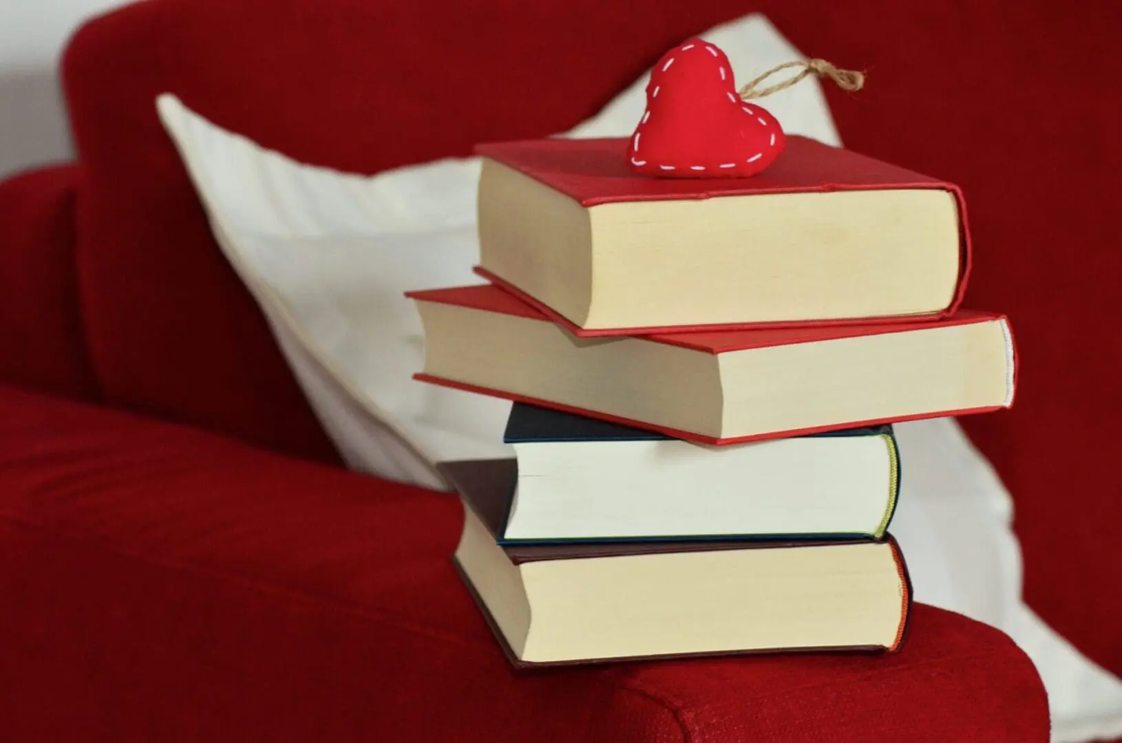 A bunch of books kept on a red couch with a heart on top of books